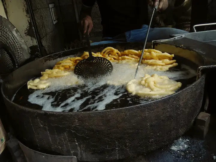 Jalebis being fried in a wide pan of hot oil