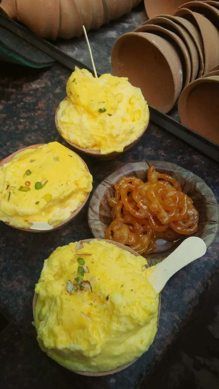 Kulhads of saffron malaiyo topped with pistachio, beside jalebi