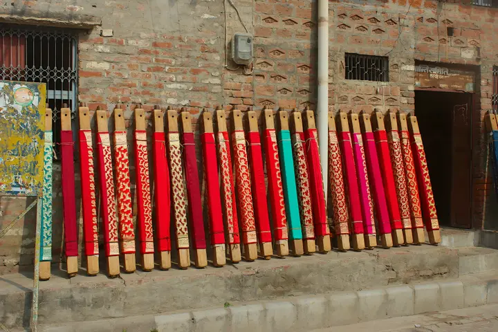 Banarasi sarees in red, pink and green with zari borders, folded on wooden display blocks outside a workshop in Varanasi