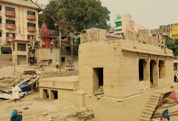 धुँधली अक्टूबर की सुबह नदी की ओर से दिखता हरिश्चंद्र घाट का पुराना बलुआ-पत्थर का मंडप, नीचे बाढ़ की गाद।