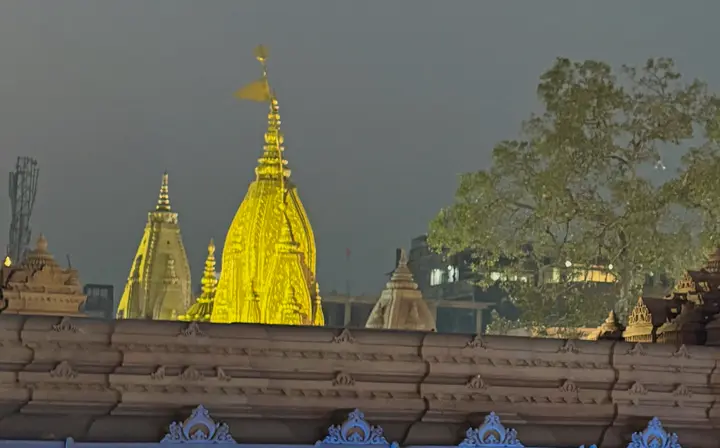Gold-plated spire of Kashi Vishwanath Temple lit at dusk above the corridor wall, Varanasi