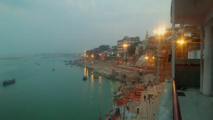 पंचगंगा घाट स्थित श्रीमठ से शाम का वाराणसी: जगमगाती सीढ़ियाँ और गंगा में तैरती नावें।